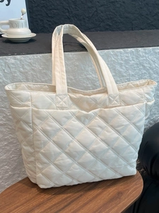 Beige quilted puffer tote bag with diamond stitching on a wooden desk for daily commute