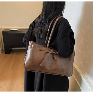 Detailed view of the large brown leather tote bag with vintage strap decor on shoulder