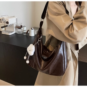 Détail du sac hobo en cuir marron foncé avec logo argenté et breloque nuage blanc