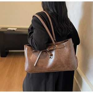 Detailed view of a vintage brown faux leather tote bag worn by a model in a minimalist room