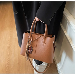 Detail of dark brown pebble leather tote bag with a checkered bear charm and tassel
