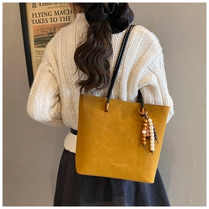 Dettaglio borsa tote giallo senape con ciondolo in legno e logo in rilievo sulla pelle