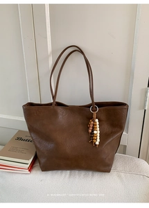 Gros plan d'un sac cabas marron caramel avec texture cuir rétro et pompon en perles