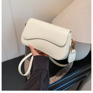 Détail du sac crème avec rabat festonné, boucle dorée et bandoulière à motifs