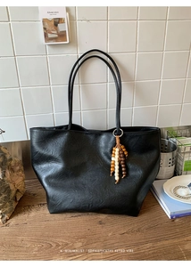 Détail d'un grand sac cabas noir avec texture cuir et pendentif en perles de bois