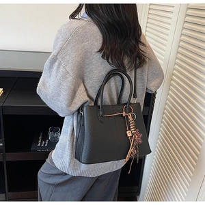 Detail of black lychee grain leather tote bag with woven charm and adjustable strap