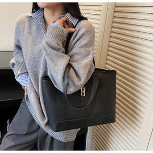 Detail of black pebbled leather tote bag featuring gold twist lock and dual handles