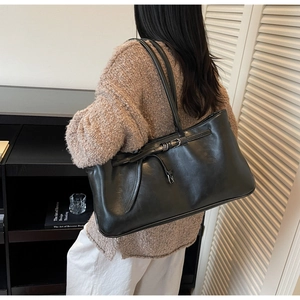 Detail showing high-capacity black tote bag in glossy synthetic leather with metal buckle