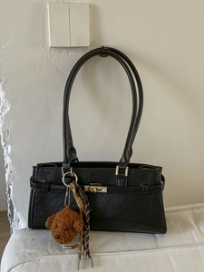 Black faux leather tote bag with gold lock and plush bear charm for daily commuting