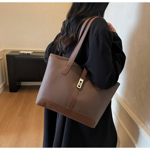 Detail of dark brown lychee leather tote bag featuring golden metal lock and strap design