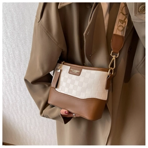 Close-up of brown leather and checkerboard fabric crossbody bag with wide shoulder strap