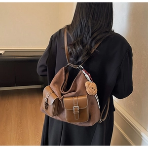 Detail of brown suede backpack with leather pockets, checkered scarf and bear charm