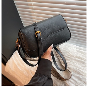 Détail du sac noir grainé avec boucle dorée et bandoulière tissée style vintage