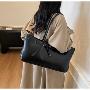 Detail of a large black tote bag with matte texture and buckle showing on a shoulder