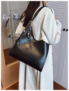 Detail of black leather tote bag with wooden bead charm on a model's shoulder