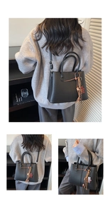 Detail of black pebbled leather tote bag with bear charm and tassel on a model