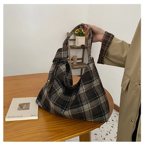 Close-up of large brown plaid wool tote bag held by model in a warm interior setting