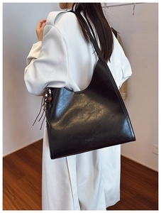 Close-up of a large black tote bag with braided tassels on a white trench coat