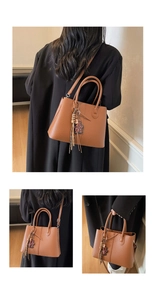 Close-up of brown litchi pattern leather tote bag with tassel and bear pendant