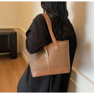 Detail of a large brown leather tote bag featuring a gold metal twist lock and dual straps