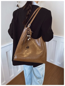 Detail of vintage brown leather tote bag featuring a decorative beaded tassel and silver buckle