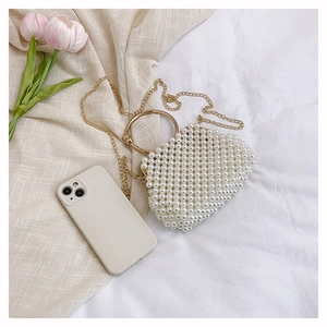 Detail of a handmade pearl beaded handbag with golden handles on a soft fabric background