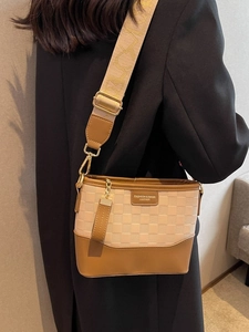 Chic checkered embossed bucket bag with wide strap worn by a model in a warm room