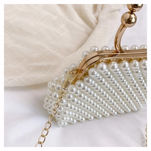 Detail of handmade pearl handbag featuring a golden metal handle and fine chain strap