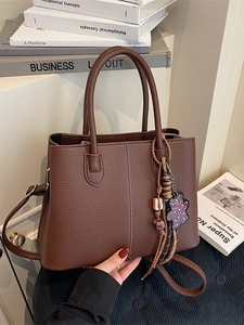 Large dark brown pebble leather tote bag with handle and charm on aesthetic books