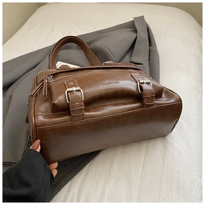 Detail of vintage brown leather pillow bag with metal buckles and textured finish