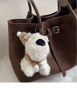 Close-up of white plush bear charm with knit hat on a brown suede tote bag