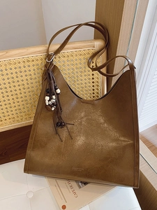 Large brown vintage leather tote bag with ethnic wood bead tassels on a stylish wooden chair