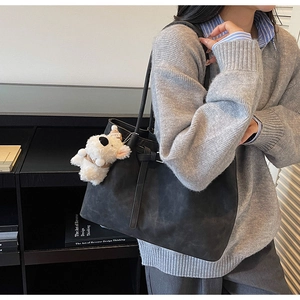 Detail of a large black tote bag with a white plush dog charm on a model in a library