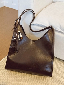 Vintage large coffee brown leather tote bag with stylish beaded tassel on white sofa