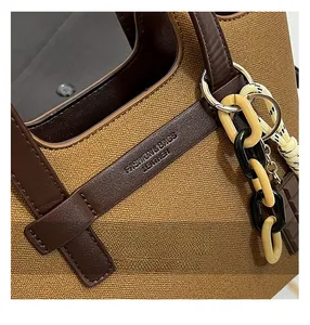 Detailed view of the brown canvas tote bag with leather straps and decorative acrylic chain