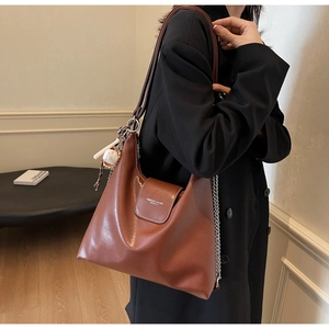 Detail of soft brown leather tote with silver chain and decorative baseball charm