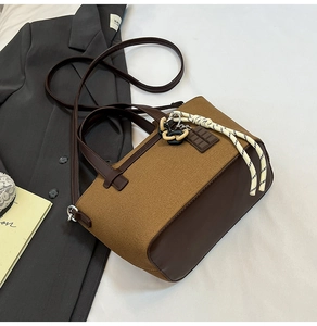 Detail of a brown canvas and PU leather crossbody bag with a woven rope charm on a bed