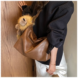 Detail of a deep brown faux leather hobo bag featuring a cute plush lion charm accessory