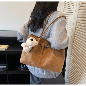 Detail of a large brown suede tote bag with cute plush puppy charm worn by a model