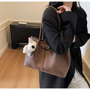 Close-up of vintage brown leather tote bag with stylish buckle and cute puppy charm