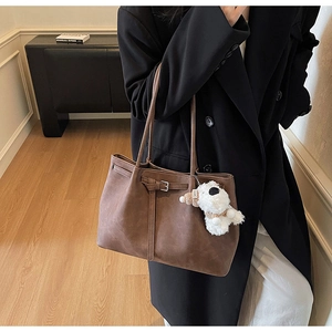 Detail of coffee brown tote bag with buckle and plush puppy charm on a model