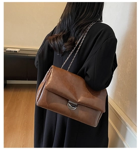 Detailansicht der braunen Leder-Schultertasche mit Metallkettenriemen an einem Modell