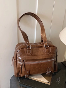 Vintage brown leather pillow bag with silver zippers on a minimalist artistic background