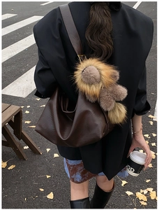 Detail of dark brown leather hobo bag with plush lion charm in an autumn street setting