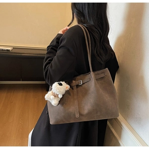 Detail of dark brown suede tote bag with side strap buckle and plush puppy charm