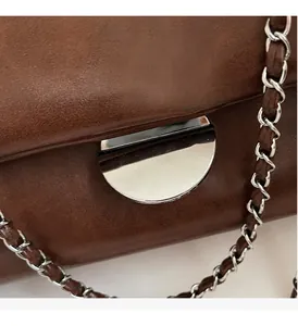 Detail der braunen Vintage-Lederhandtasche mit silberner Halbrundschnalle und Kettengurt
