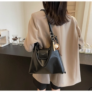 Detail of black soft leather tote bag with white stitching and baseball charm on model