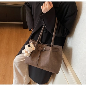Detail of dark brown tote bag with leather buckle straps and cute white plush bear pendant