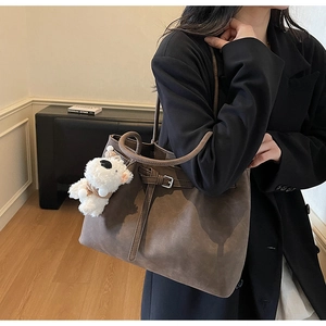 Detail view of large brown vintage tote bag with buckle strap and plush dog keychain