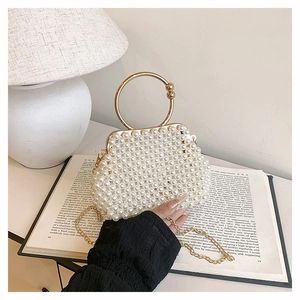Detail of elegant pearl handbag featuring golden circular handle on an open book